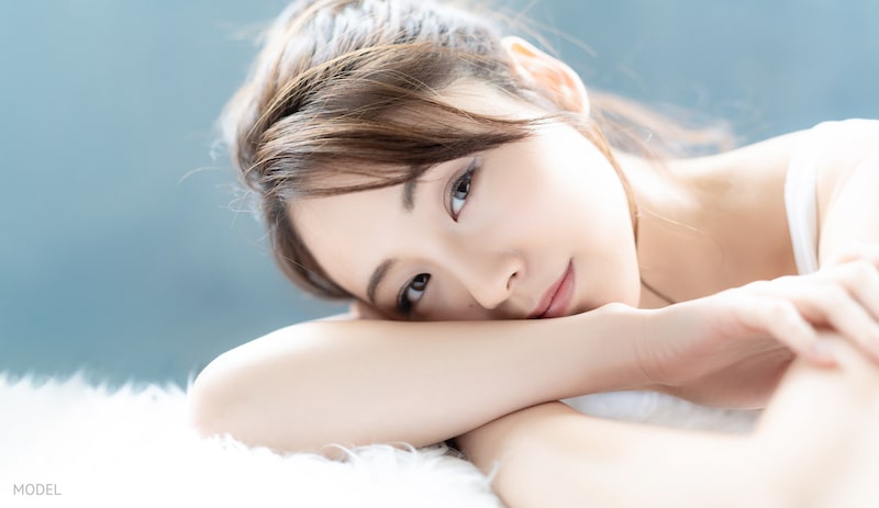 Asian woman with beautiful acne-free skin with face resting on arm.