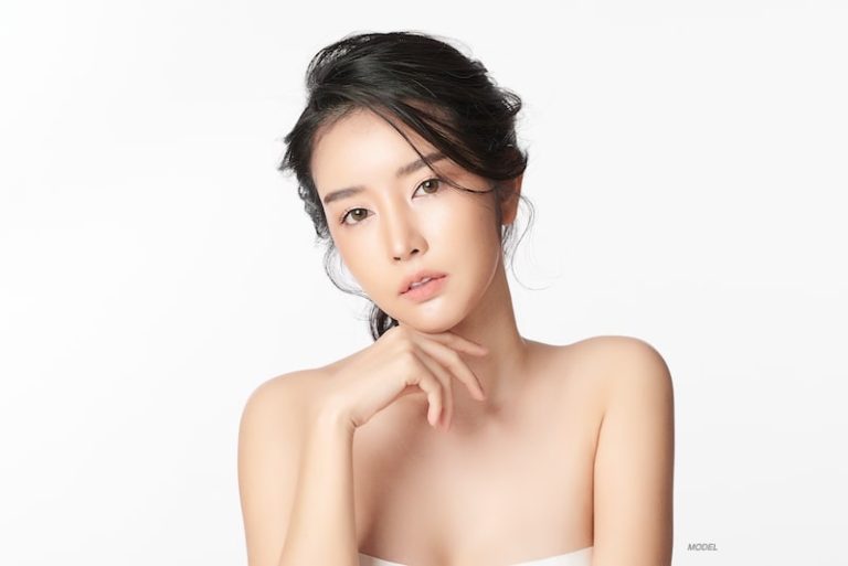Beautiful young Asian woman gazes at camera with her hand under her chin